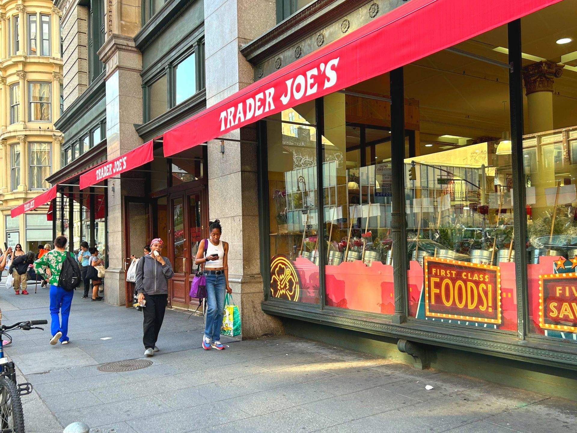 TRADER JOE'S 간판이 있는 상업 건물과 도로를 지나는 사람들의 모습