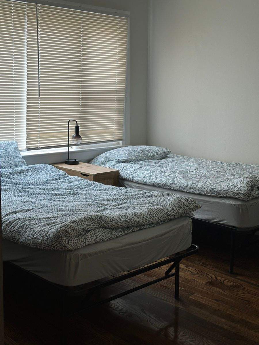블라인드가 설치된 창문 아래 두 개의 침대와 나무 소재의 테이블이 있는 방