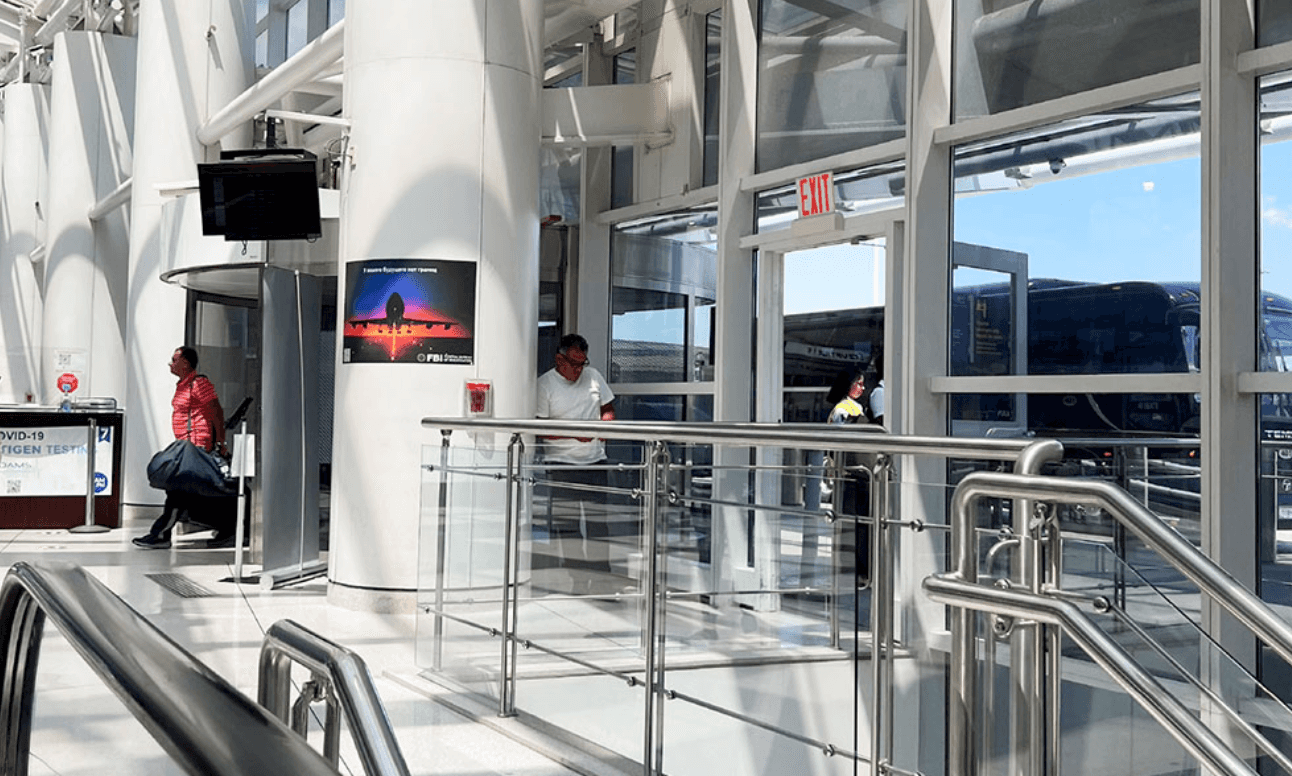 공항 건물 내부에 투명 패널로 된 계단과 유리창이 있는 공간, 사람과 간판이 보입니다