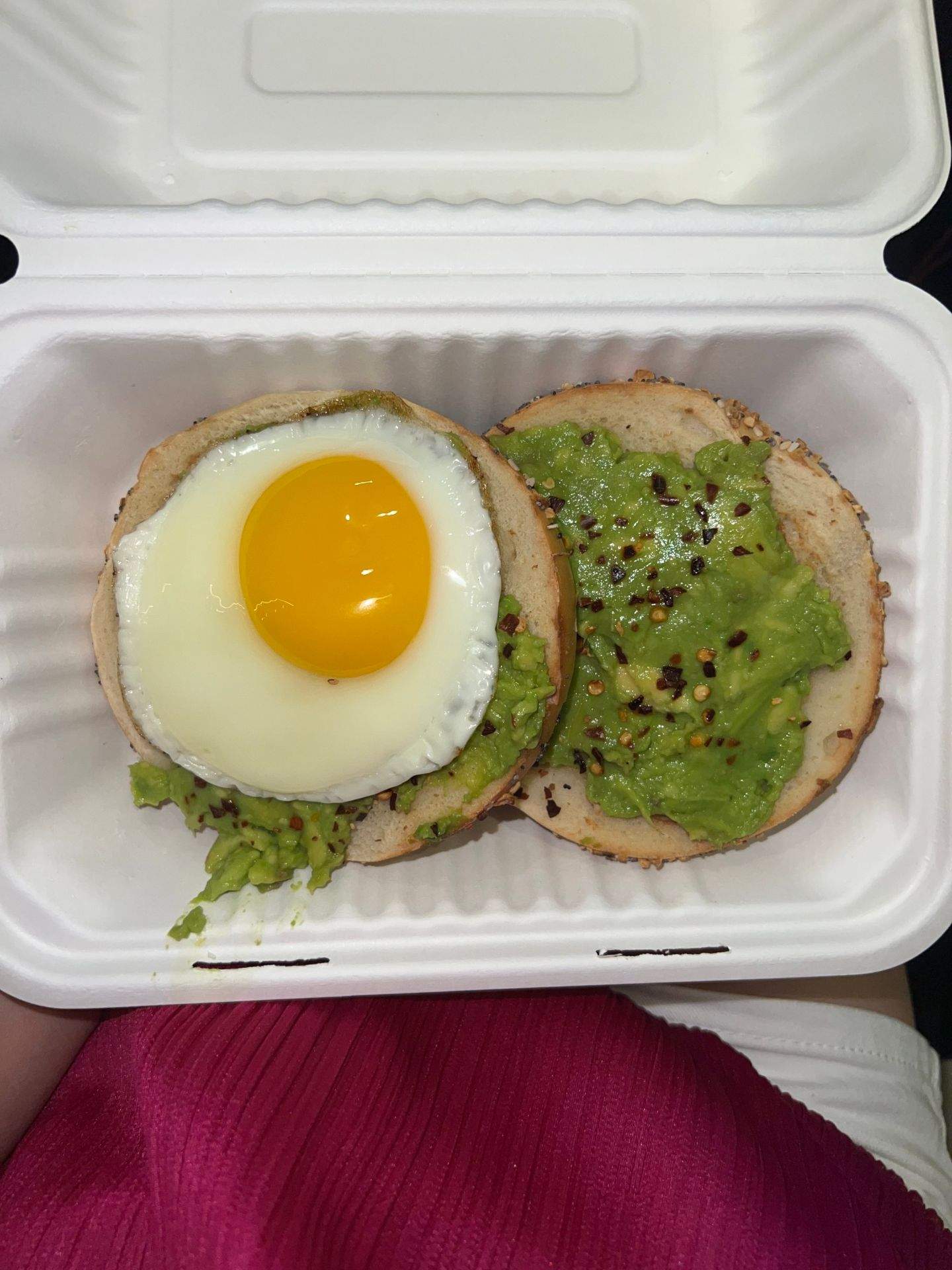 흰색 플라스틱 용기에 담긴 빵 위에 아보카도 페이스트와 계란이 올려져 있는 모습