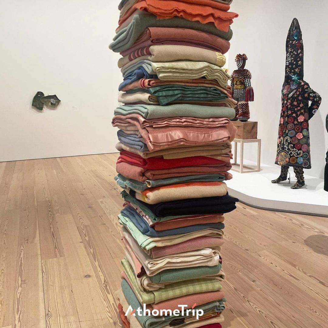 흰 벽과 목재 바닥이 있는 전시 공간에 놓인 여러 가지 색상의 옷과 인형