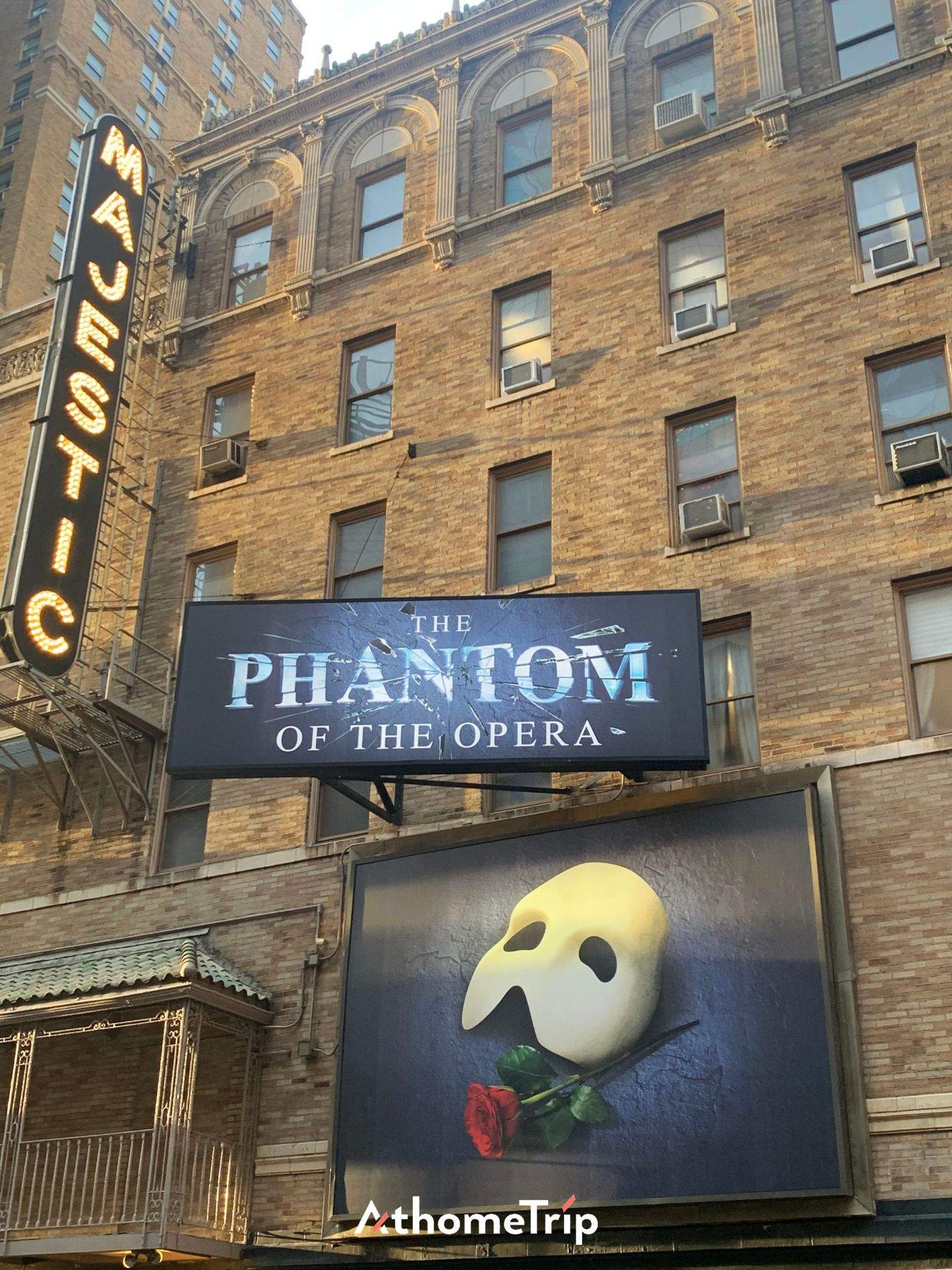 도시 건물 외벽에 THE PHANTOM OF THE OPERA 문구가 적힌 공연 광고판과 간판이 보이는 장면