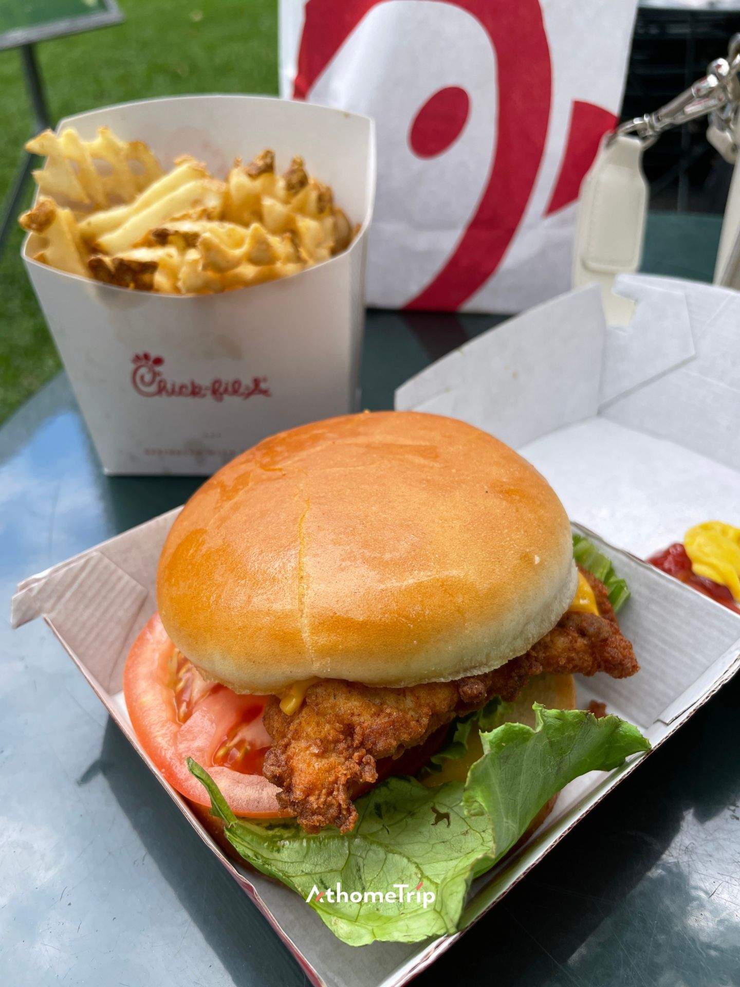 Chick-fil-A 로고가 보이는 야외에서 종이 상자에 담긴 버거와 치즈 웨이퍼가 놓여 있는 모습