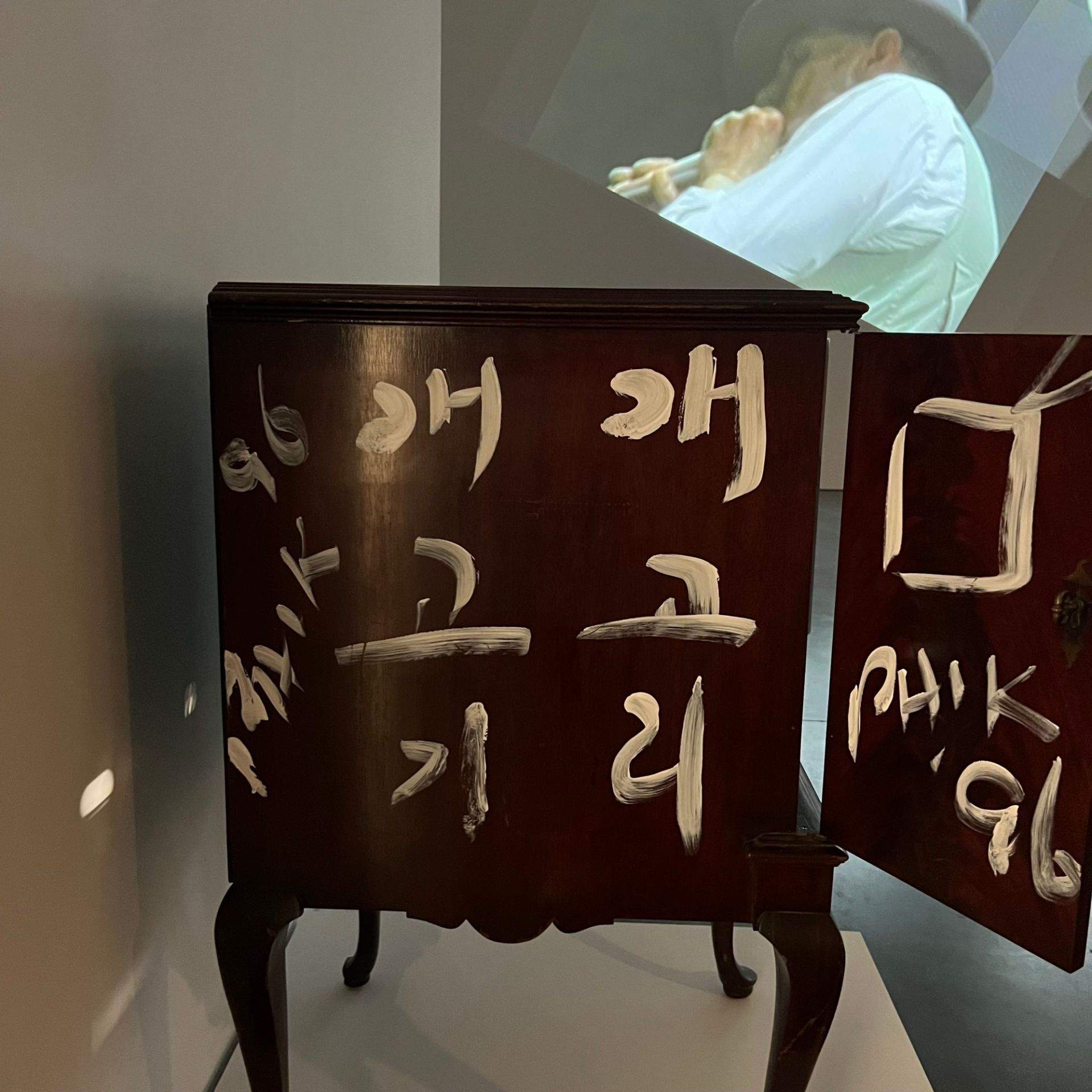문이 열려 있고 표면에 흰색 글씨가 쓰인 전시 공간 내 목재 서랍장