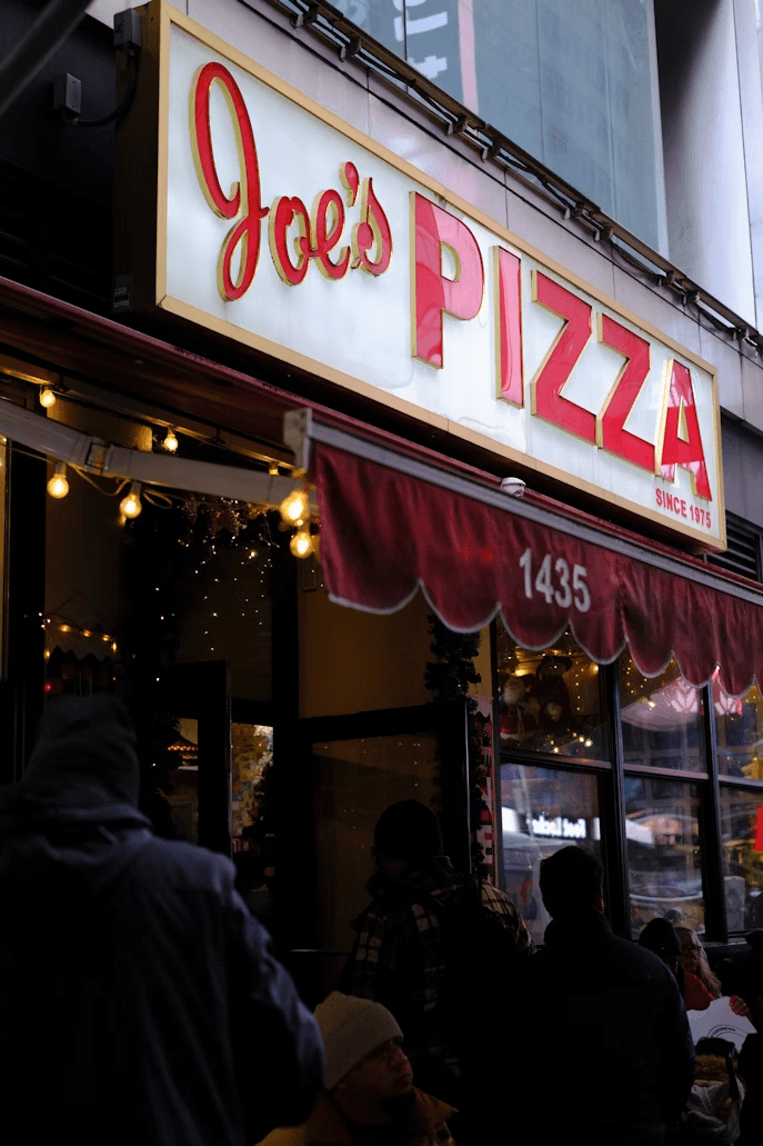 Joe's PIZZA라는 글자가 적힌 간판과 가게 앞에 있는 사람들의 모습