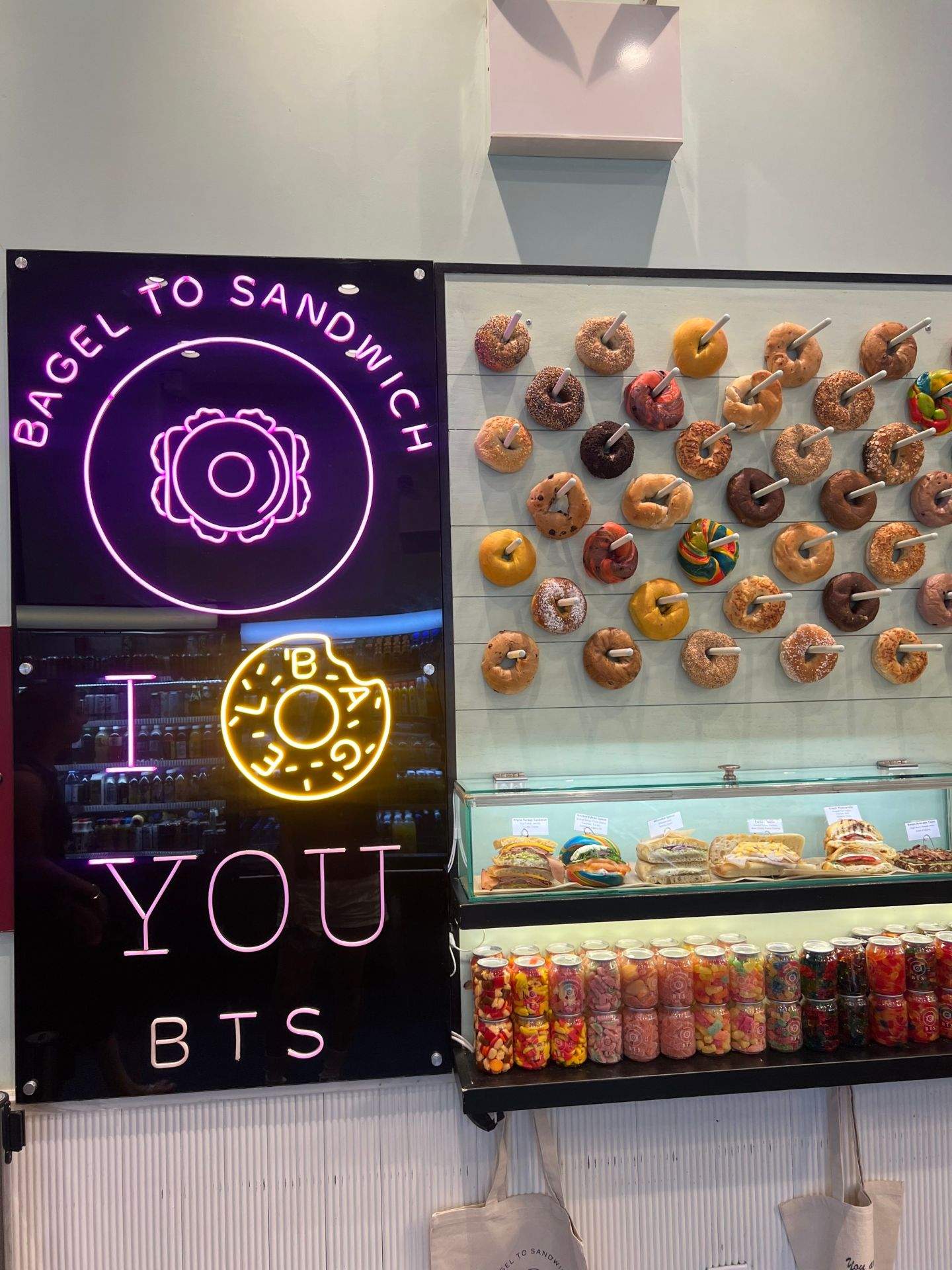 BAGEL TO SANDWICH 문구가 적힌 전광판과 도넛, 캔 음료 등 간식이 진열된 실내 모습