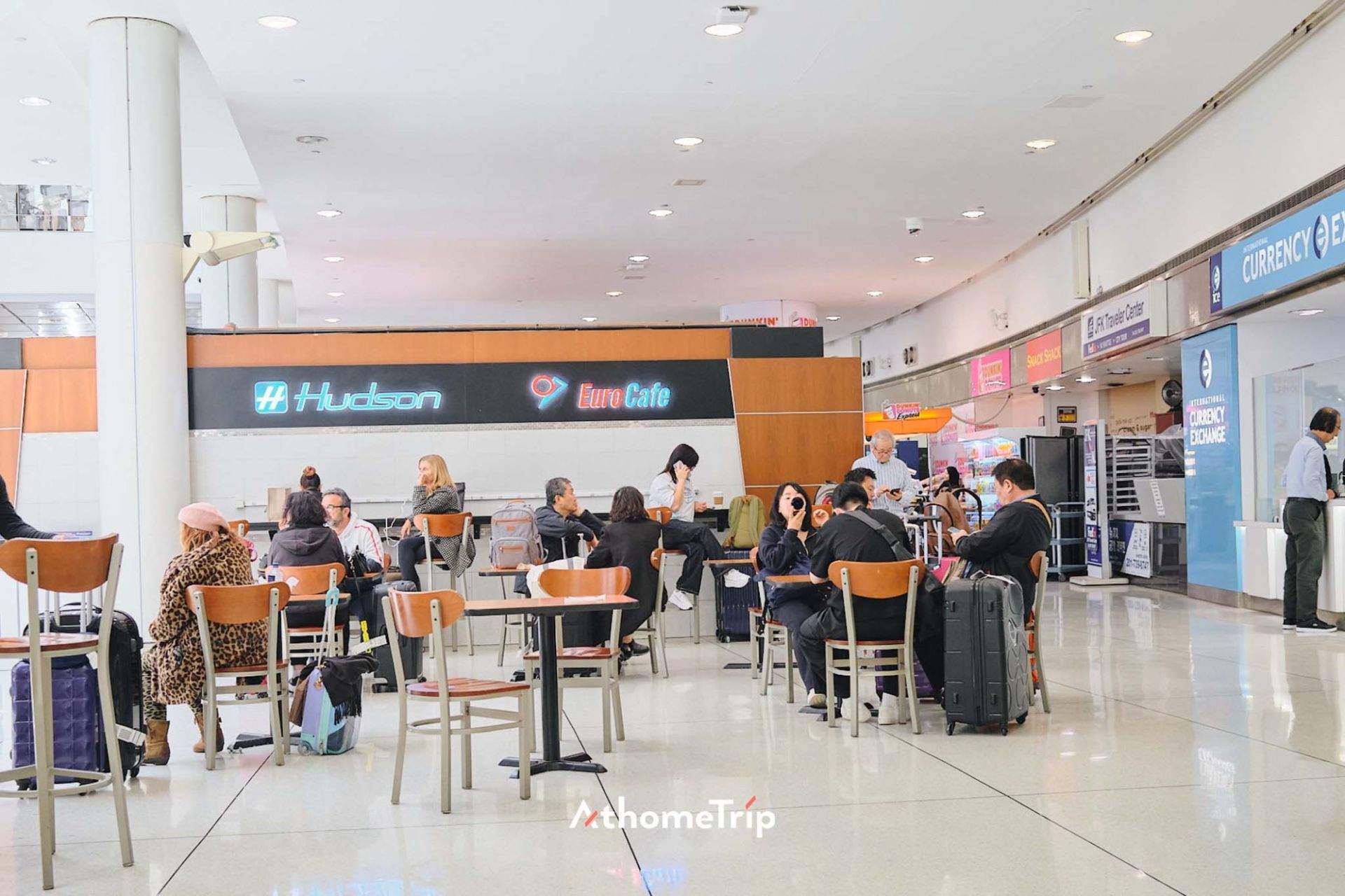 공항 휴게실에 여러 사람과 의자, 테이블, 가방 등이 배치된 장면